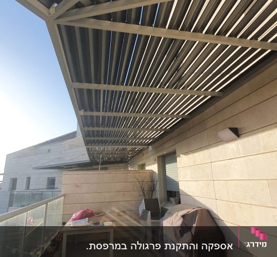 פרגולה מתכתית מעל מרפסת עם שולחן וכיסוי גריל